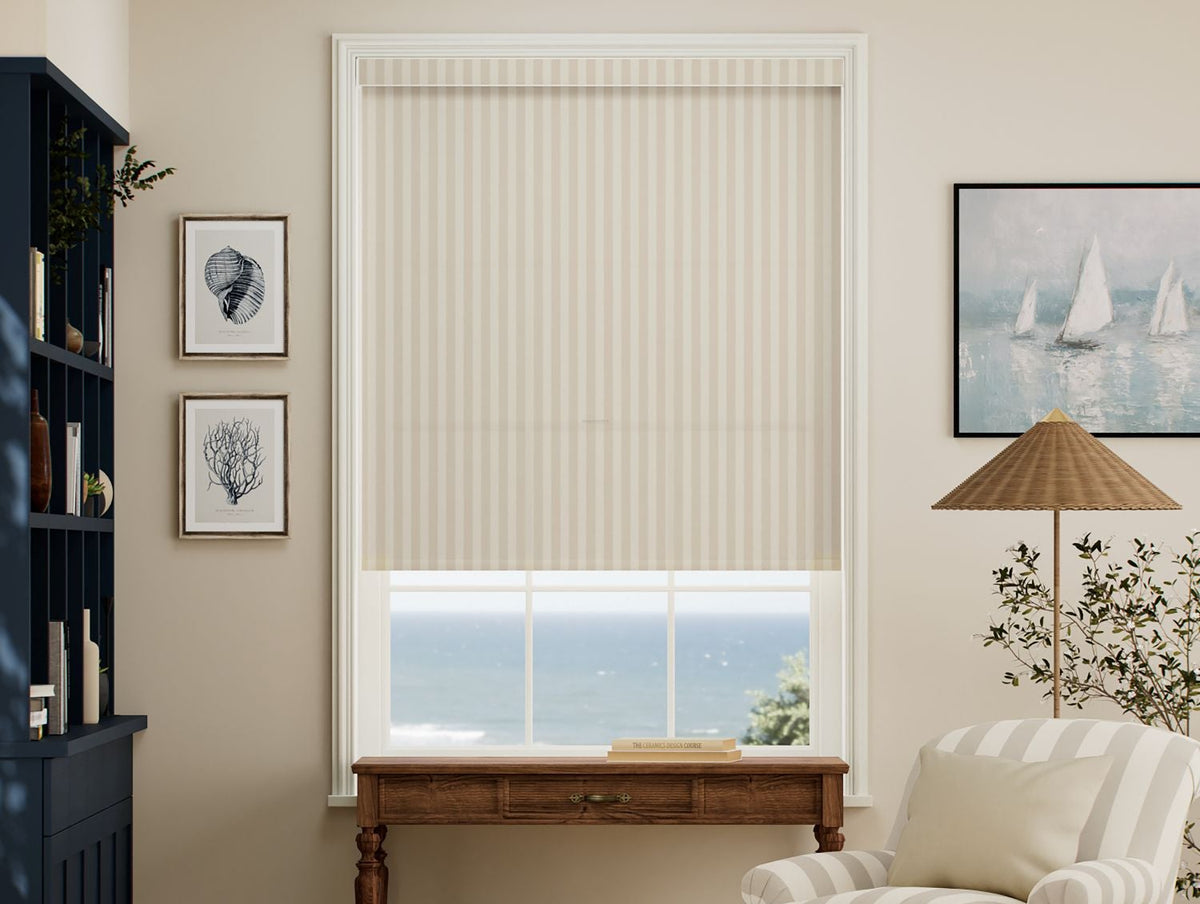A beige roller shade with vertical stripes, partially drawn over a window in a styled living room with an ocean view.