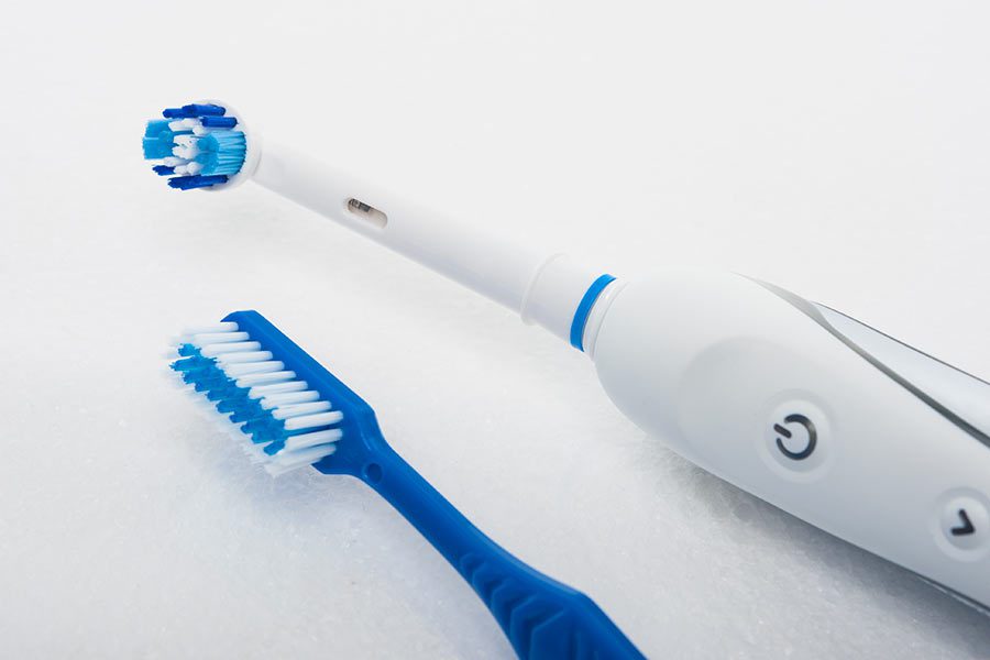 White and blue electric motorized tooth brush next to standard blue toothbrush
