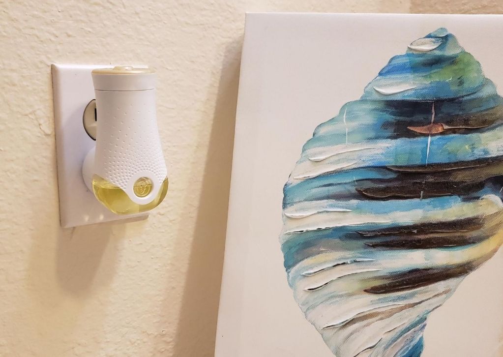 Air freshener plugged into a wall outlet next to a painting of a shell.