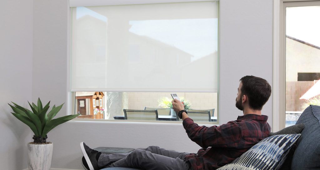 Man on living room couch using remote control operated window blinds